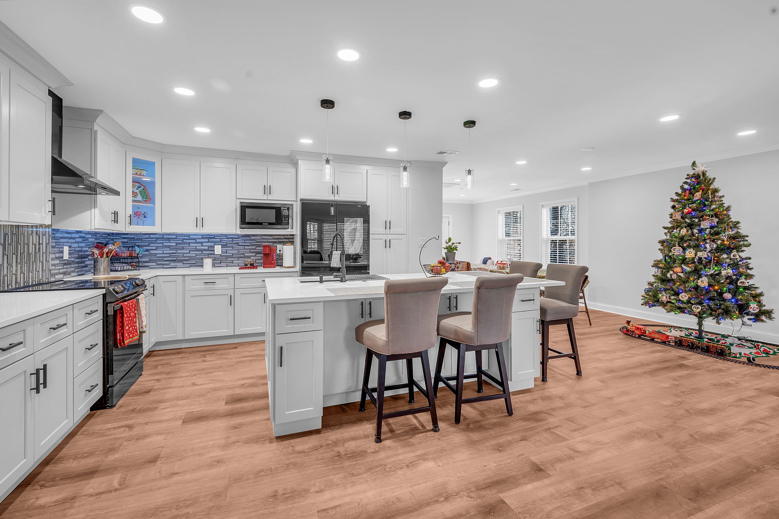 pacious kitchen and dining area in a room addition by Mosaic Design & Build, featuring white cabinetry, stainless steel appliances, blue tile backsplash, and hardwood floors, with a decorated Christmas tree adding a festive touch to the room in Fairfax
